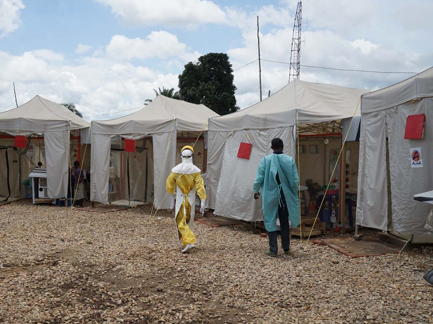 Two people wearing personal protective equipment walk through medical tents
