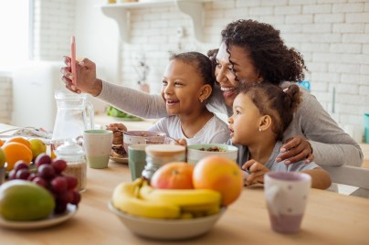 Dark-skinned woman standing near her daughters while taking selfie photo with her two daughters