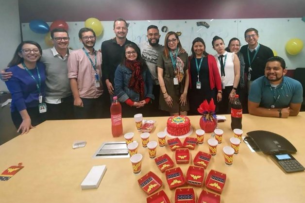 colleagues standing behind large table with cake in the middle having a celebration