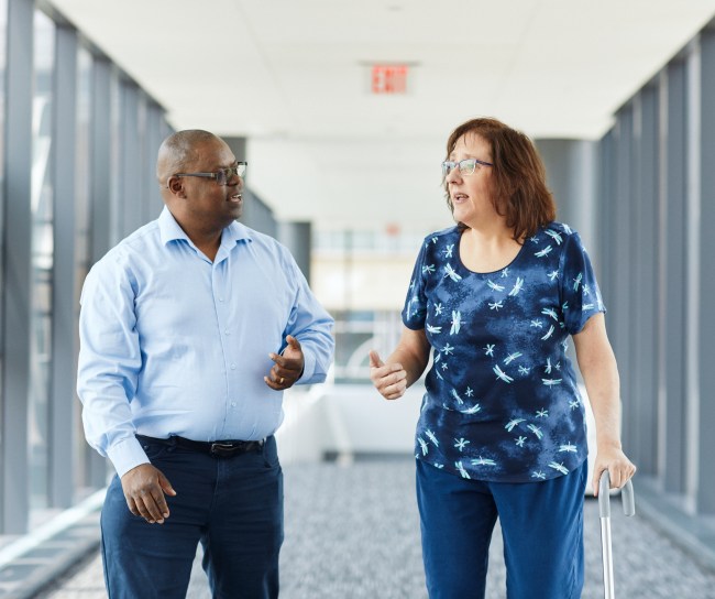 man and woman walking in the office. The woman has a cane.