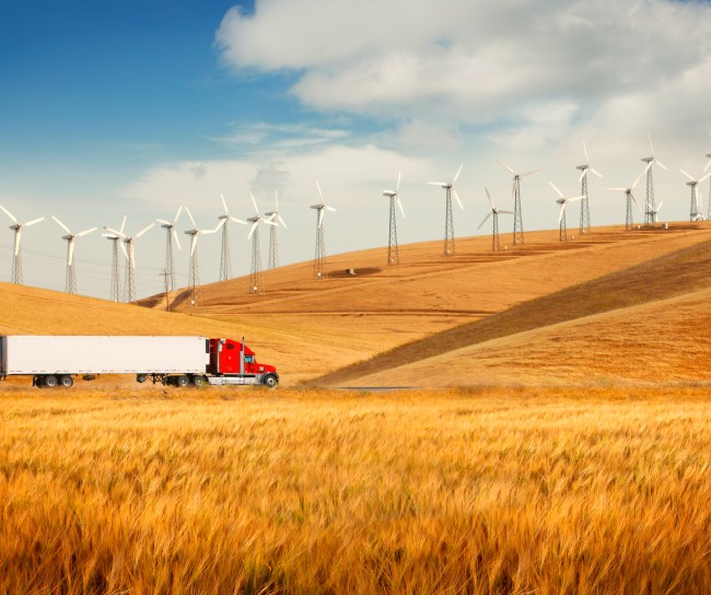 Truck traveling through wheat field with wind mills