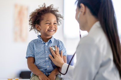 toddler smiling while female doctor listens to his heart with a stethoscope