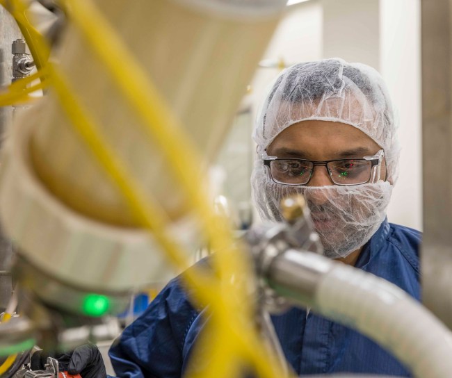 Man wearing hair net and mask working in a manufacturing facility
