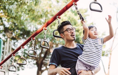 Adult holding a child while she hands on monkey bar