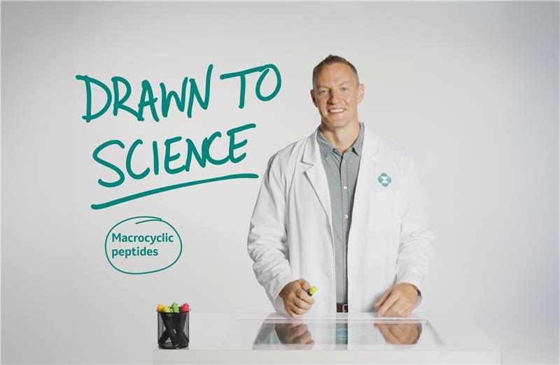 man wearing white coat standing next to text reading drawn to science